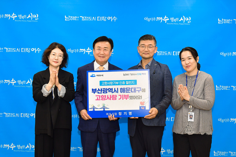 여수시청에서 고향사랑기부 인증 챌린지 행사에 참석한 정기명 여수시장이 해운대구에 기부한 내용을 담은 현수막을 들고 있다. 참석자들이 함께 기념사진을 찍고 있다.