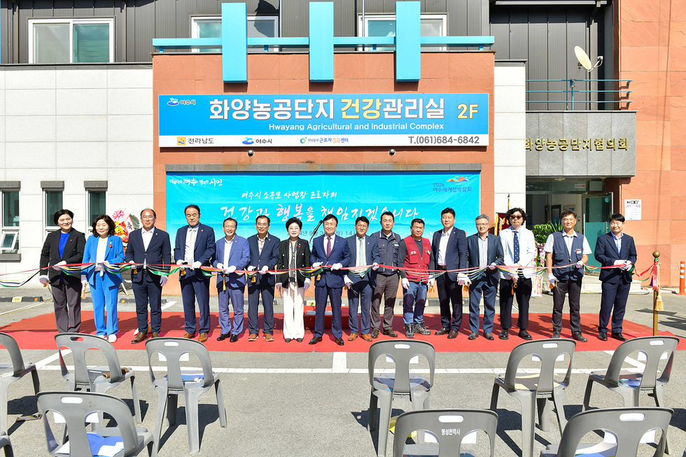 여수시 화양농공단지 건강관리실 개소식에서 여러 인사들이 리본을 자르고 있다. 배경에는 건강관리실과 관련된 현수막이 걸려 있다.