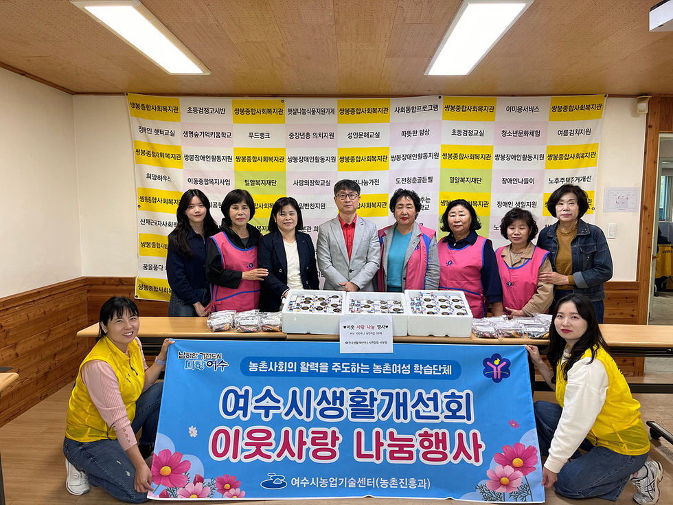 여수시생활개선회 회원들이 이웃사랑 나눔행사를 진행하며 기념사진을 찍고 있다. 배경에는 행사 관련 현수막과 여러 기관 이름이 적혀 있다.