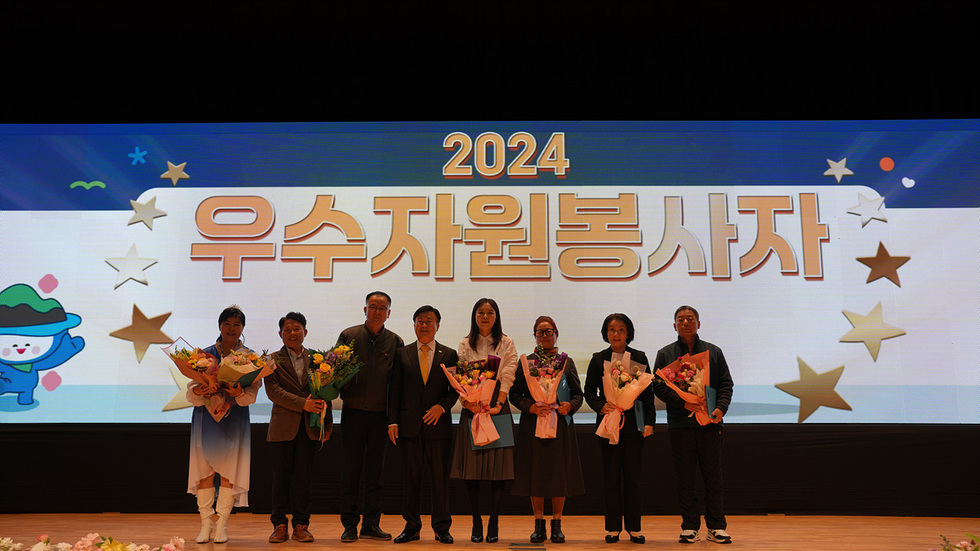 2024 우수자원봉사자 시상식에서 수상자들이 꽃다발을 들고 기념사진을 찍고 있다.