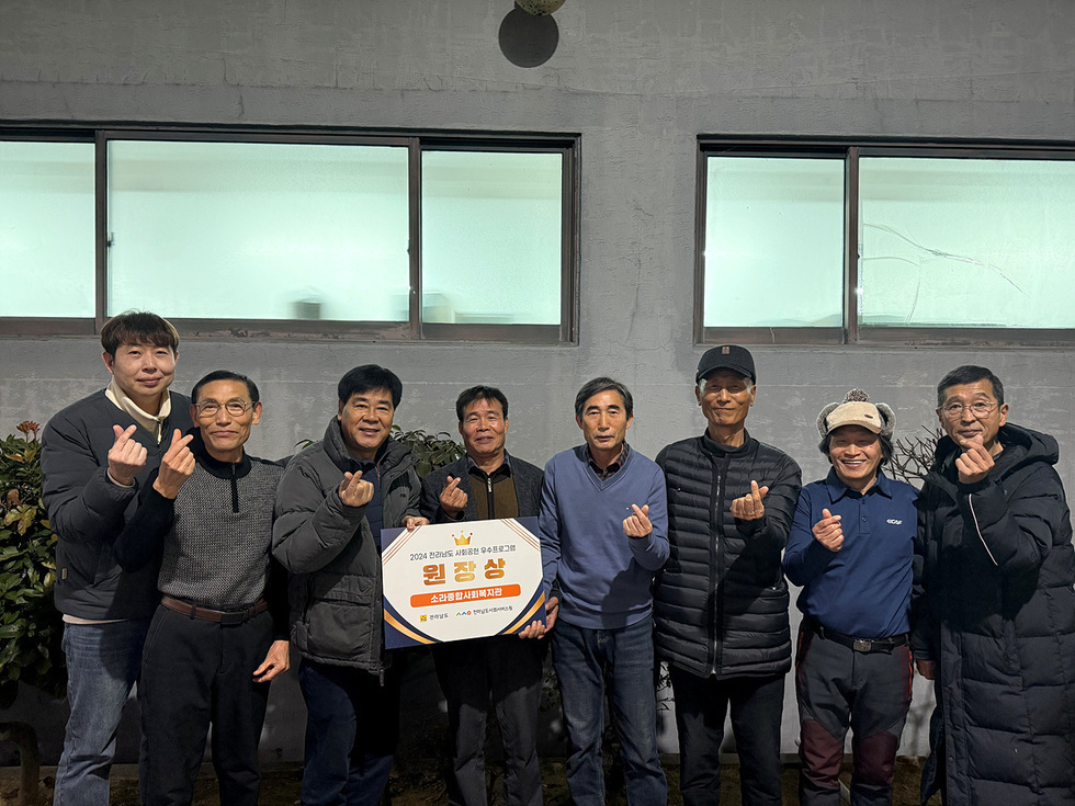 여러 남성이 상을 들고 손가락 하트를 만들며 기념사진을 찍고 있는 모습이다. 배경에는 창문과 식물이 보인다.