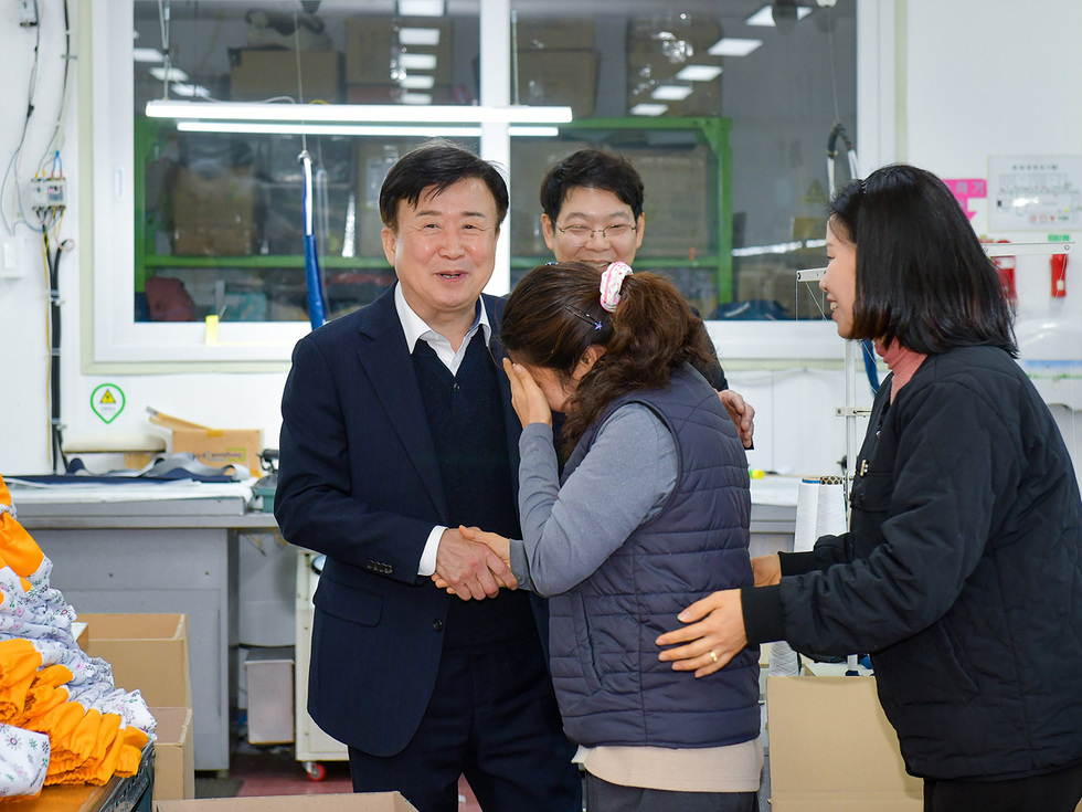 한 남성이 여성과 악수하며 대화하고 있고, 다른 여성은 감정이 북받쳐 눈물을 흘리고 있다. 배경에는 작업 공간과 상자들이 보인다.