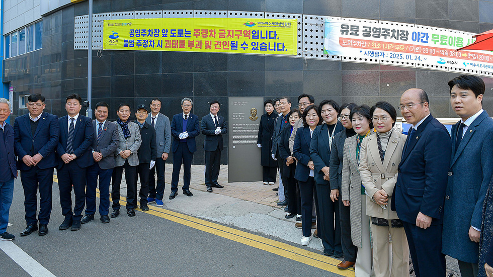 여수시 공영주차장 앞에서 여러 사람들이 모여 있는 모습으로, 주정차 금지 안내문과 유료 주차장 이용 안내가 보인다.