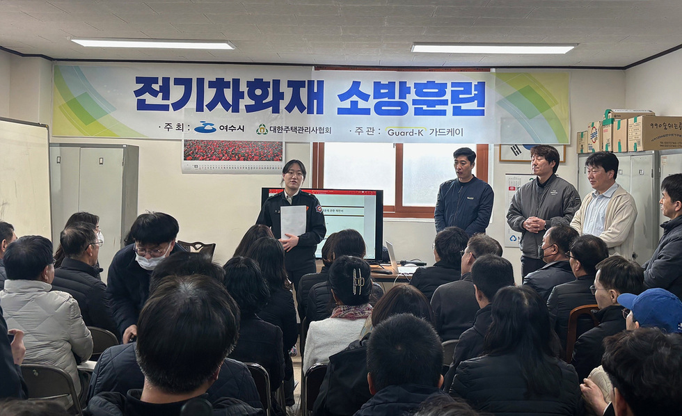 여수시에서 전기차 화재 소방훈련이 진행되고 있으며, 강사가 교육을 하고 있다. 참석자들이 강의를 경청하고 있다.