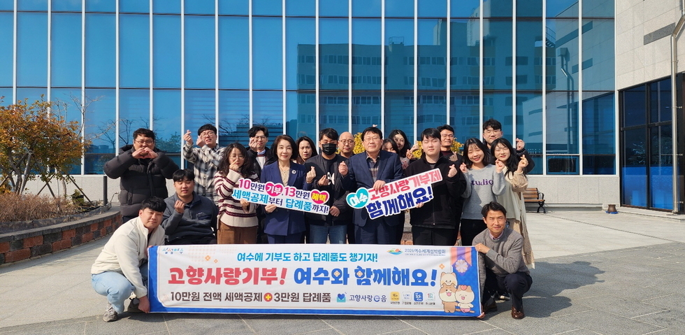 여수에서 고향사랑기부 캠페인에 참여한 사람들로, 여러 명이 모여 기념사진을 찍고 있다. 현수막에는 기부와 관련된 내용이 적혀 있다.