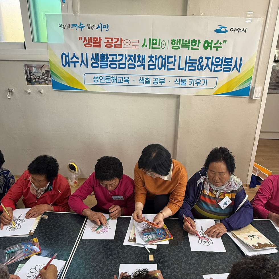 여수시에서 노인들이 색칠 공부를 하며 자원봉사 활동에 참여하는 모습이다. 배경에는 여수시의 생활공감정책 관련 현수막이 걸려 있다.