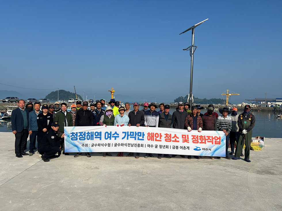 여수 가막만 해안에서 청소 및 정화작업에 참여한 사람들과 함께 현수막을 들고 있는 모습