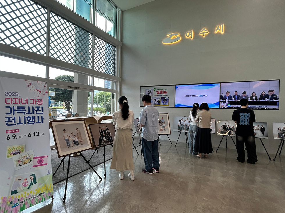 여수시에서 다자녀 가정의 가족사진 전시행사가 열리고 있으며, 관람객들이 사진을 감상하고 있다.