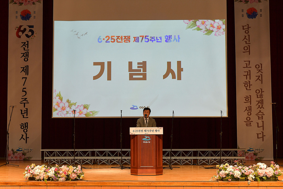 6·25전쟁 제75주년 행사에서 기념사를 하는 남성이 무대에 서 있다. 배경에는 행사 제목이 적힌 화면과 꽃 장식이 보인다.