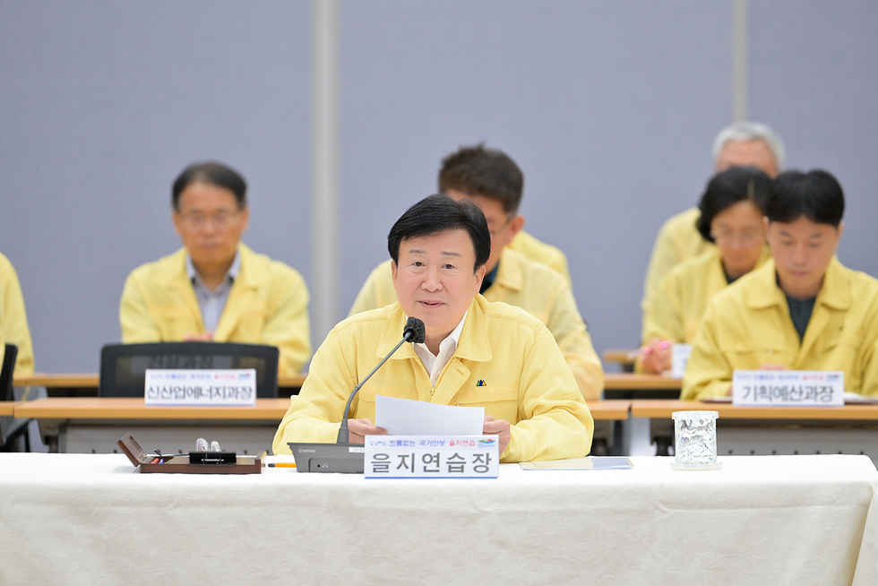 을지연습장에서 회의를 진행하는 모습으로, 앞에 앉은 남성이 발언하고 있으며, 뒤에는 여러 명의 참석자가 보인다.