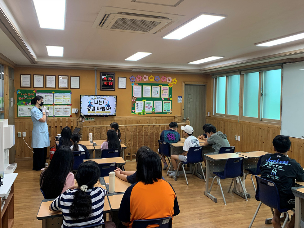 교실에서 강사가 학생들에게 청결에 대해 설명하고 있으며, 학생들은 강의를 듣고 있다.