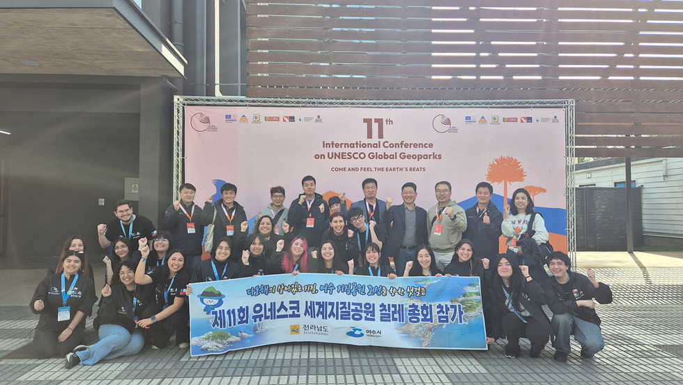 칠레에서 열린 제11회 유네스코 세계지질공원 총회 현장에서 참가자들이 현수막을 펼쳐 들고 단체 기념촬영을 하며 손을 들어 환영의 포즈를 취하고 있는 모습.