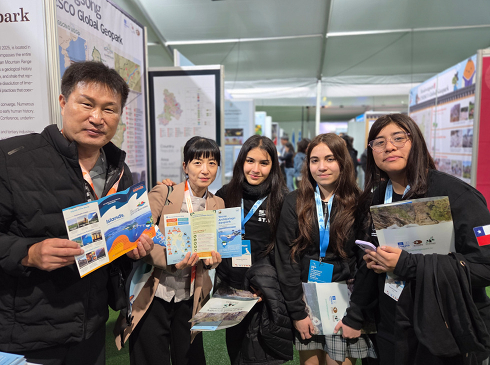여수시 관계자와 외국 참가자들이 지질공원 관련 홍보 책자를 들고 함께 서서 설명과 안내를 나누며 카메라를 향해 미소 짓고 있는 모습.