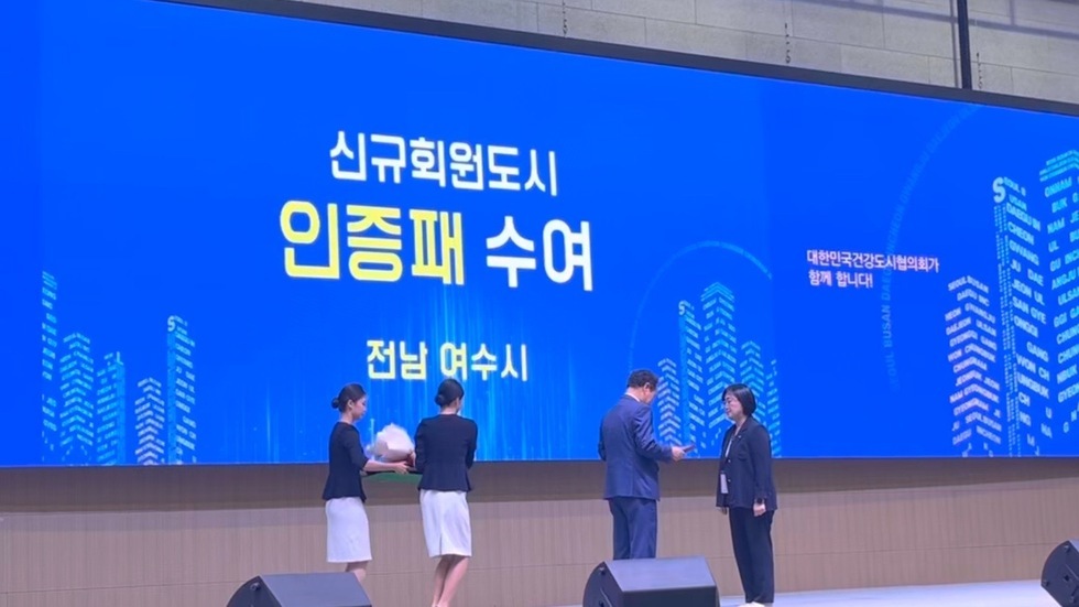 여수시가 대한민국건강도시협의회에서 신규회원 도시 인증패를 수여받는 장면으로, 행사에서 관계자들이 인증패를 교환하고 있다.