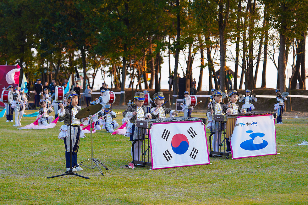 여수마칭페스티벌에서 어린이 마칭밴드가 연주를 펼치고 있는 모습. 어린이들이 반짝이는 제복을 입고 태극기와 여수시 로고가 그려진 악기 앞에서 힘차게 연주하고 있다