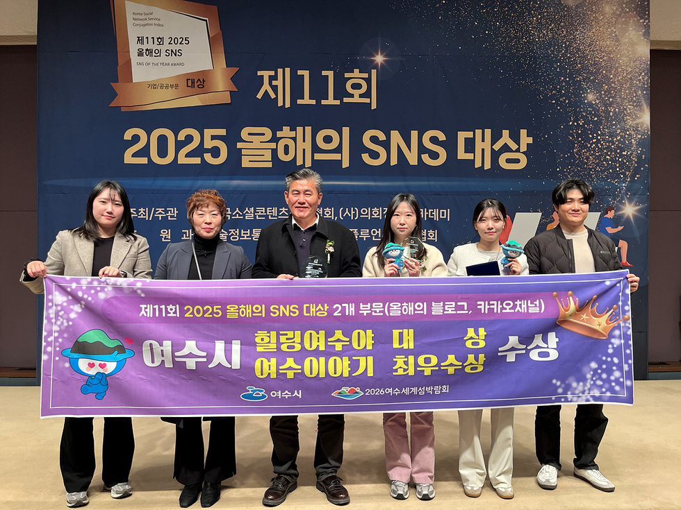 2025 올해의 SNS 대상’ 시상식 현장에서 여수시 관계자들이 수상 배너를 펼쳐 들고 기념촬영하는 모습. '힐링여수야 대상'과 '여수이야기 최우수상' 문구가 적힌 보라색 현수막을 들고 있으며, 뒤편에는 시상식 배경막이 설치된 무대가 보인다