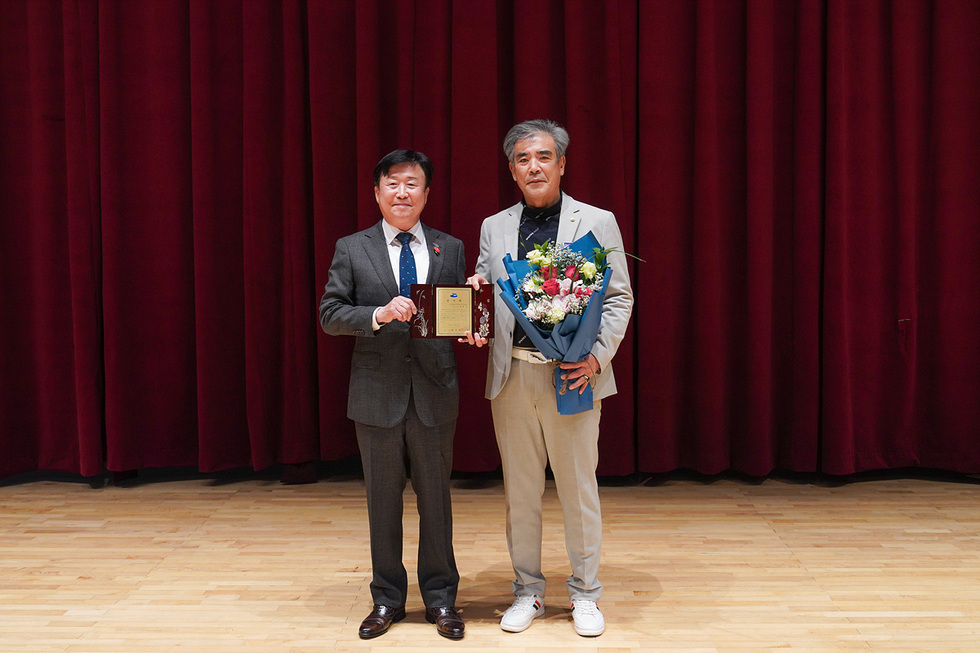 붉은 커튼이 배경인 실내 무대에서 정기명 여수시장과 임동성 전임 협의회장이 나란히 서서 기념 촬영을 하고 있는 모습. 왼쪽 인물은 감사패를 들고 있고, 오른쪽 인물은 꽃다발을 들고 있으며 두 사람 모두 시상식에서 수상한 듯 단정한 복장을 하고 있다