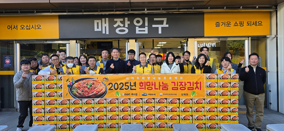 이마트 여수점 매장 입구 앞에서 노란 조끼를 착용한 봉사자들과 관계자들이 김장김치 상자를 쌓아 놓고 희망나눔 김장김치 전달 행사 기념사진을 찍고 있는 모습. ‘2025년 희망나눔 김장김치’라고 적힌 현수막이 상자 위에 걸려 있다.