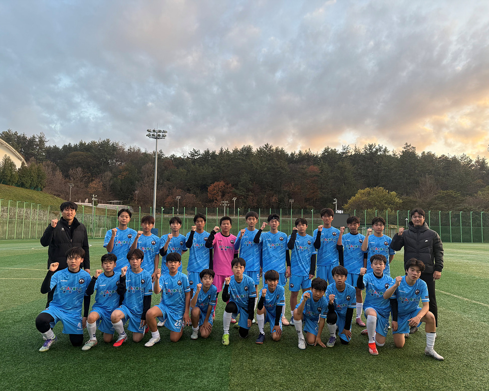 축구 경기장 잔디 위에서 여수해양FC U-15 선수단과 코치진이 파란색 유니폼을 착용한 채 단체로 서서 주먹을 쥐고 포즈를 취하며 기념촬영하는 모습