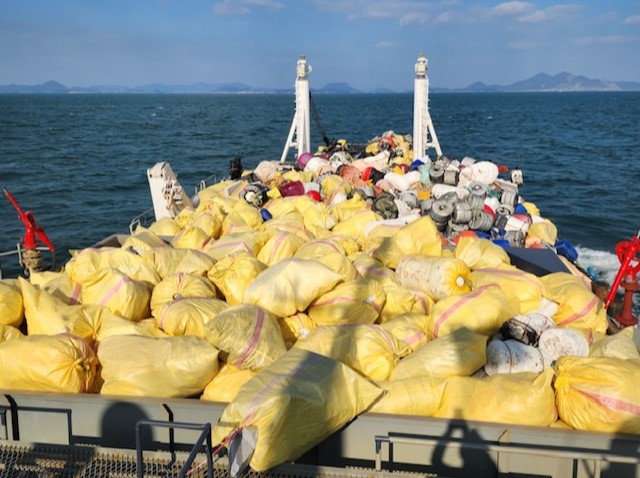 해양쓰레기 수거 작업을 마친 정화선이 바다 위를 운항 중인 모습. 배 위에는 노란 자루와 스티로폼 부표 등 수거된 해양쓰레기가 가득 적재되어 있으며, 주변으로 여수 바다와 섬들이 보인다