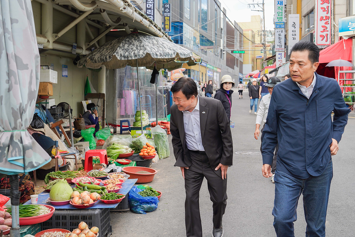 정기명 여수시장이 전통시장 골목을 걸으며 노점에서 판매 중인 채소와 농산물을 살피고 상인과 인사를 나누는 현장 행보 모습.