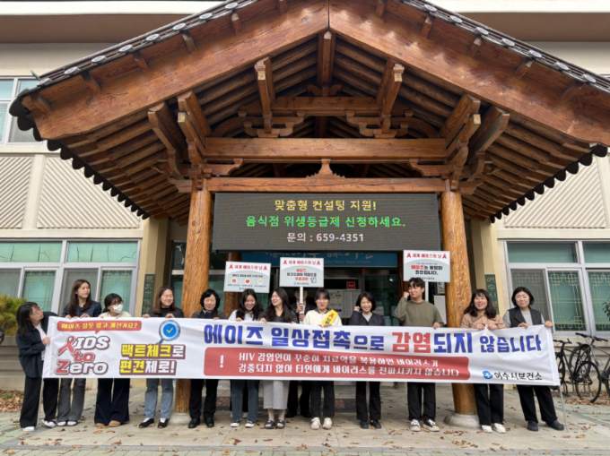 여수시보건소 관계자들과 시민들이 건물 앞에서 ‘세계 에이즈의 날’ 홍보 캠페인에 참여해 한 줄로 서서 현수막을 들고 있다. 현수막에는 “에이즈 일상접촉으로 감염되지 않습니다”, “팩트체크로 편견제로!” 등이 적혀 있다. 참석자들은 예방수칙 안내 피켓을 함께 들고 있으며, 건물 전광판에는 ‘맞춤형 컨설팅 지원! 음식점 위생등급제 신청하세요’ 문구가 표시돼 있다.