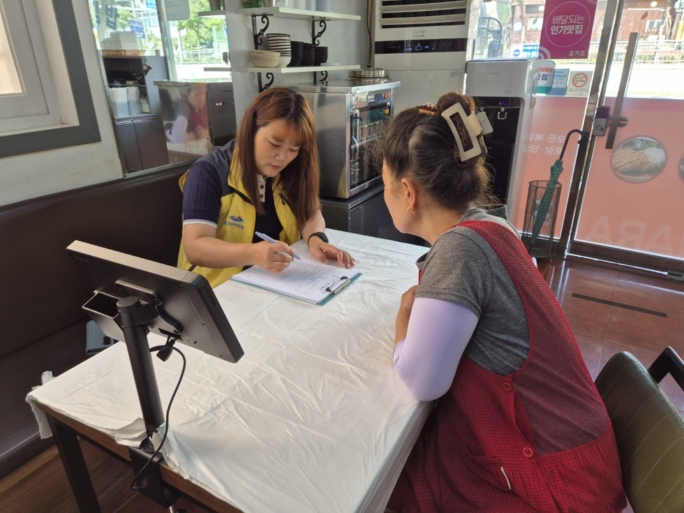식당 내부에서 공무원 직원이 서류에 기록하며 음식업소 실태조사를 진행하고 있는 모습