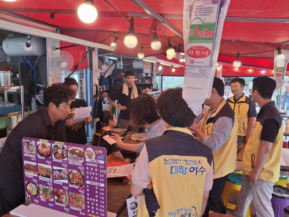 여수시 단속반 직원들이 노란 조끼를 입고 음식점을 방문해 업주에게 1회용품 사용 규제와 과태료 안내 등 특별 점검 사항을 설명하고 있는 모습