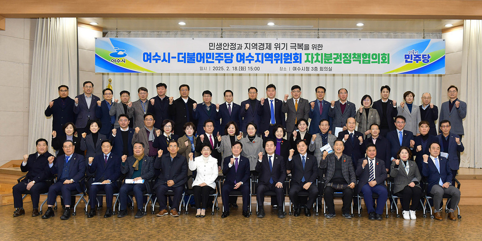 여수시청에서 더불어민주당 여수지역위원회 자치분권정책회의가 열리고 있으며, 참석자들이 주먹을 쥐고 포즈를 취하고 있다.