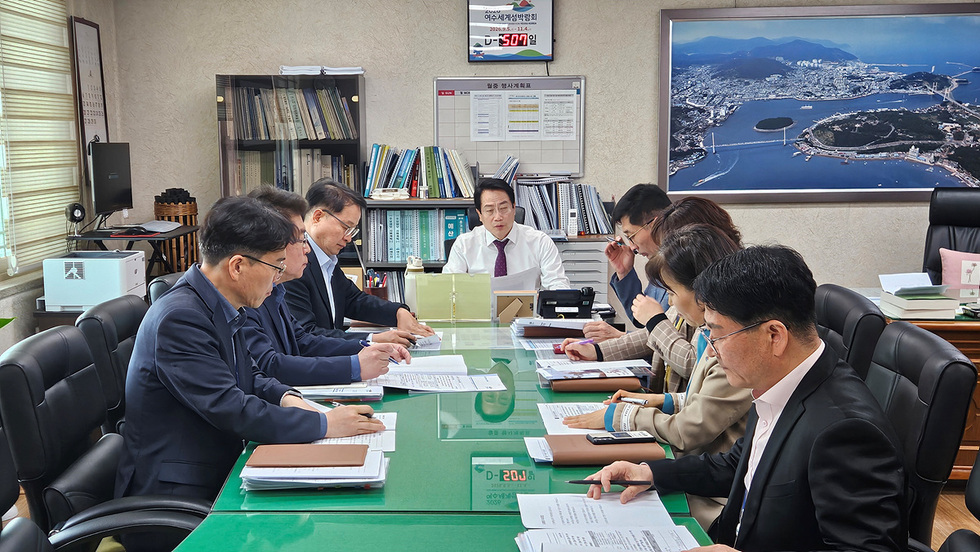 여수시청 회의실에서 여수세계섬박람회 관련 회의가 진행되고 있는 모습으로, 여러 명의 참석자들이 테이블에 앉아 문서 작업을 하고 있다.