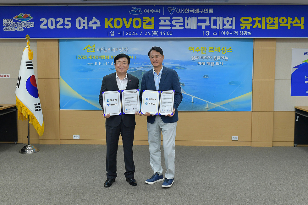 여수시청 상황실에서 2025 여수 KOVO컵 프로배구대회 유치협약식이 열리고 있으며, 두 사람이 협약서를 들고 서 있다.