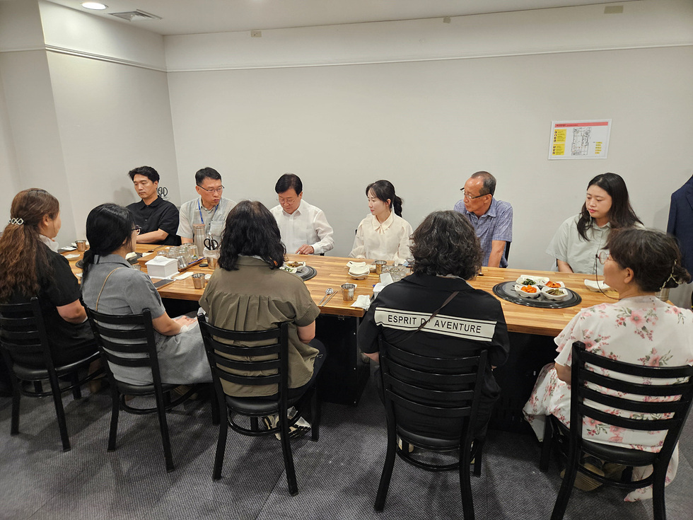 여러 사람이 식탁에 앉아 식사를 하고 있는 장면으로, 남성과 여성 여러 명이 대화를 나누고 있다.