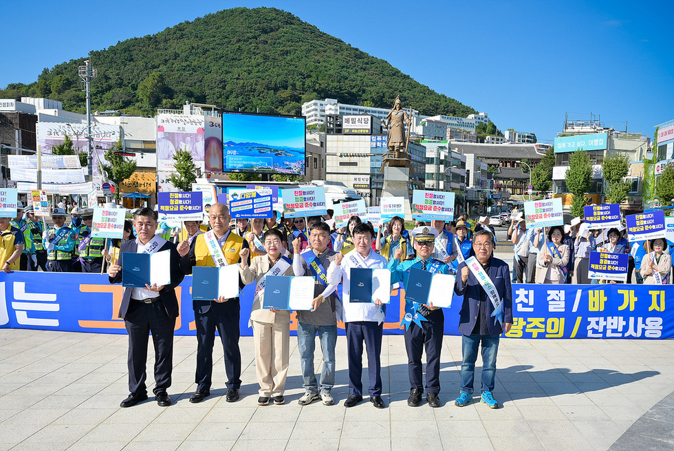 여수시 이순신광장에서 친절관광 캠페인에 참여한 200여 명의 사람들이 친절한 응대와 청결한 환경 조성을 홍보하며 손을 들고 있다.