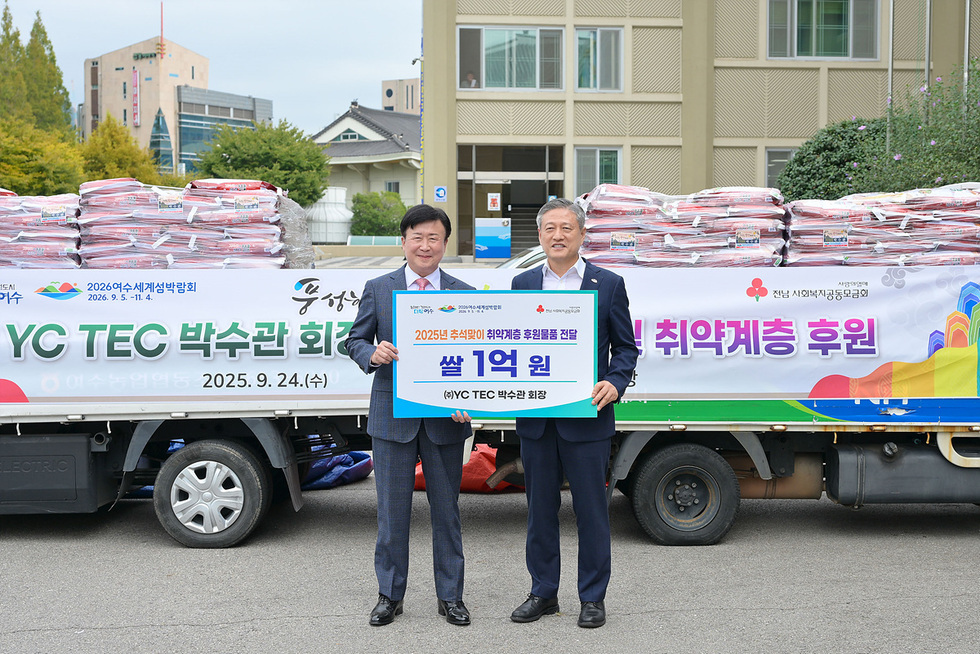 여수시청 앞에서 박수관 회장이 정기명 시장과 함께 쌀 1억원 기탁식을 진행하고 있다. 배경에는 기탁된 쌀이 쌓여 있다.