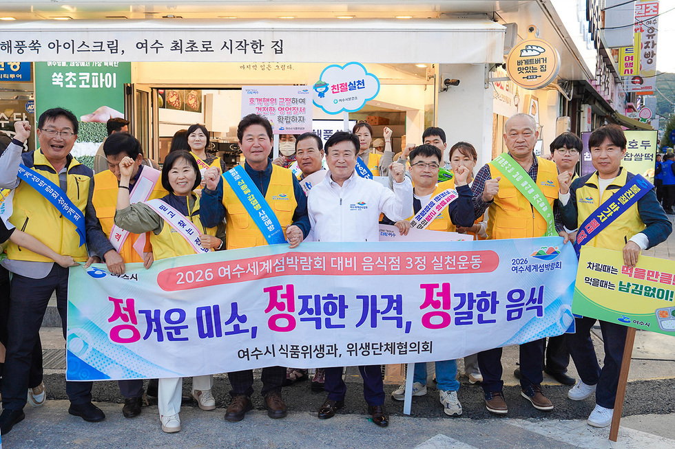 여수시에서 열린 2026 여수세계섬박람회 대비 음식점 실천운동 행사에서 정기명 여수시장과 시민들이 현수막과 판넬을 들고 구호를 외치고 있다.