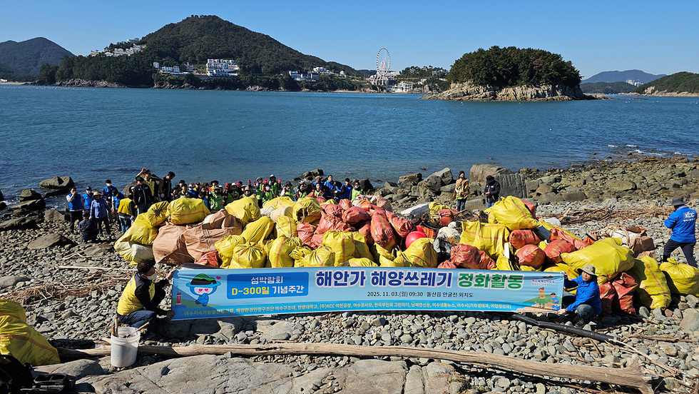 여수 돌산 안굴전 외치도 해안가에서 시민들이 해양쓰레기 정화활동을 벌이며 수거한 쓰레기 자루들이 쌓여 있는 모습 섬박람회 D-300 기념주간 해안가 해양쓰레기 정화활동 2025년 11월 3일(월) 09:30 돌산읍 안굴전 외치도라고 적힌 현수막이 보인다.