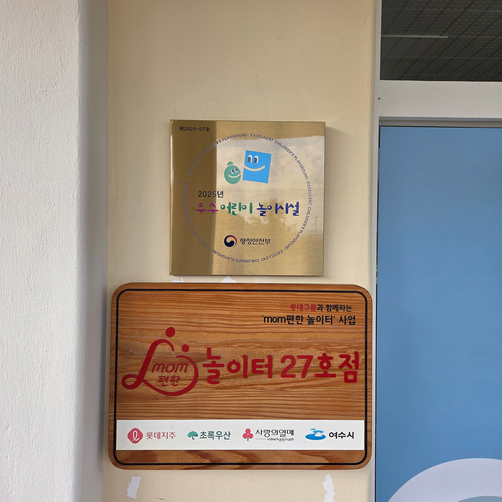 행정안전부가 인증한 ‘2025년 우수 어린이놀이시설’ 현판과 ‘mom편한 놀이터 27호점’ 명패가 나란히 부착된 여수시 공공형 실내놀이터 출입문 입구 모습