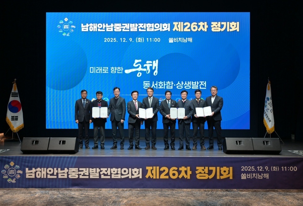남해안남중권발전협의회 제26차 정기회 행사장에서 여러 시·군 대표자들이 무대에 나란히 서서 협약서(문서)를 펼쳐 보이며 기념촬영을 하고 있다. 뒤편 대형 스크린에는 ‘해안남중권발전협의회 제26차 정기회’, ‘2025.12.9.(화) 11:00 쏠비치남해’, ‘미래로 향한 동행, 동서화합·상생발전’ 문구와 행사 일시·장소가 표시되어 있다.